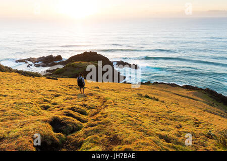 Une personne sur un promontoire herbeux observe le lever du soleil sur la mer et un beau littoral en Australie. Banque D'Images