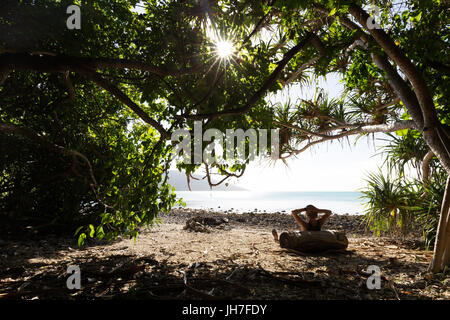 Une personne s'appuie contre un journal et se détend à l'ombre d'un arbre, hors de la chaleur du soleil, sur une belle plage tropicale en Australie. Banque D'Images