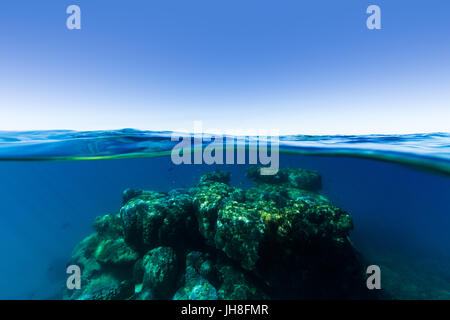 Un sous plus de split shot d'un récif corail sortant de profondeur, eau bleu clair sur une journée ensoleillée sur la Grande Barrière de Corail. Banque D'Images