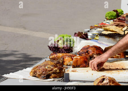 Rôti d'agneau et de porc haché. La main d'un homme atteint de quelques morceaux de viande. Salade verte, vinaigrettes, plats d'visible dans l'arrière-plan flou. Banque D'Images