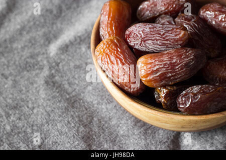 Dates fraîches Medjool dans bol en bois dans le coin supérieur droit, fond gris foncé. Focus sélectif. Banque D'Images