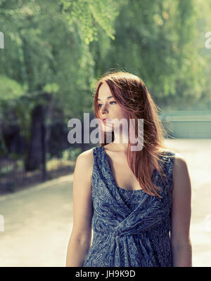 Image aux couleurs d'une femme aux cheveux rouge se détendre dans un parc. Banque D'Images