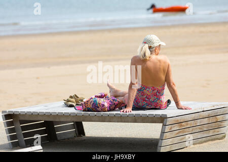 Bain de soleil femme alors que dans un maillot de bain sur un transat sur la célèbre station balnéaire de Colwn Bay dans le Nord du Pays de Galles Banque D'Images