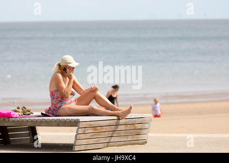 Bain de soleil femme holding et de parler sur un téléphone mobile alors que dans un maillot de bain sur un transat sur la célèbre station balnéaire de Colwn Bay dans le Nord du Pays de Galles Banque D'Images