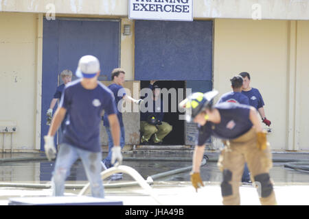 San Diego, CA, USA. Le 13 juillet, 2017. Pompier de San Diego, Mike Hall, accroupie arrière regarde les pompiers junior qu'ils contrôle flexible pratique en face de l'intérieur à la construction d'attaque Fire-Rescue Centre de formation. Le San Diego Fire-Rescue Ministère a organisé un premier pompier Junior Camp au centre de formation off Fire-Rescue Kincaid Road près de l'extrémité ouest de Lindbergh Field. Les garçons et filles âgés de 10''"16 ont été invités à participer à cette semaine de camp et apprendrez à utiliser des flexibles et des échelles, de recherche et de sauvetage contre l'incendie premiers soins de base et des compétences. Il y a un total de Banque D'Images