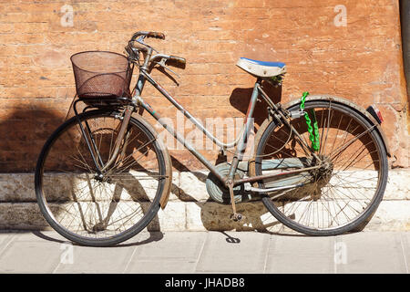 Un vieux, rouillé vélo blanc avec un panier appuyé contre un mur grungy en Italie. Banque D'Images