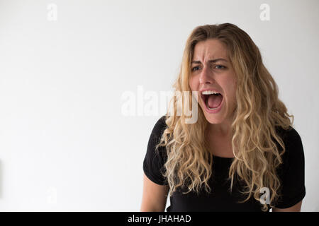 Jeune, blonde, caucasian woman exprime les émotions négatives, colère, criant et finger pointing at viewer et photographe sur un fond blanc. Banque D'Images