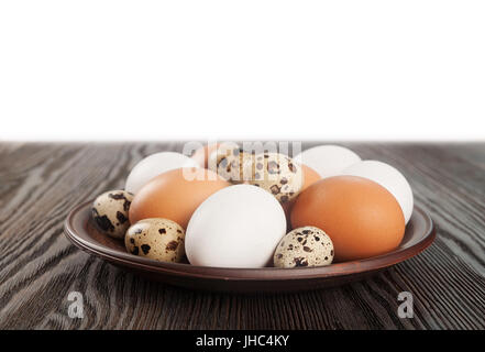 Les cailles et oeufs de poule dans une plaque d'argile sur une table en bois Banque D'Images