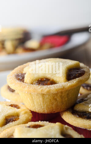 Une pile de petits pâtés de Noël avec étoile forme feuilletée toppers en premier plan. Une plaque à tarte en partie mangé, serviette et fourchette dans soft focus background Banque D'Images