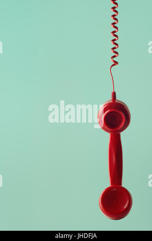 Un British 60s et 70s style retro téléphone rouge récepteur, face à l'avant et suspension par cordon en spirale à l'aqua l'arrière-plan. Banque D'Images