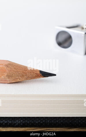 De près de l'extrémité d'un crayon dessin au graphite en bois au bord d'un carnet de croquis vierge page avec sharpener in soft focus arrière-plan. Banque D'Images