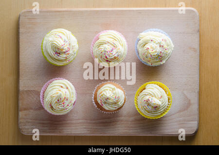 Vue de dessus de façon décorative et glacé six cupcakes en silicone de dentelle en papier ordinaire et de cas. Planche à découper en bois placées sur une table Banque D'Images