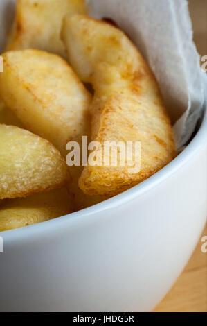 Close up of chips cuits (frites), servi dans un bol en céramique blanche avec une serviette en papier sur une table en bois clair. Banque D'Images