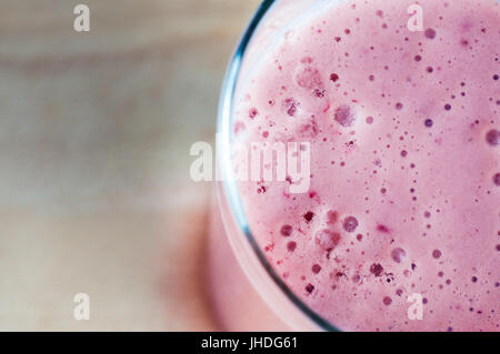 Frais généraux en angle close up d'un smoothie rose mousseuse à base de fruits d'été et le lait de soya. Comité permanent sur le bois qui fournit l'espace de copie de flou à la Banque D'Images