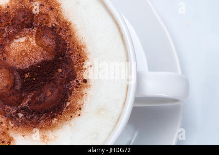 Coup de frais généraux de mousse de lait et le cacao de la mise d'une latte ou un cappuccino au café de style tasse blanche avec soucoupe. Banque D'Images