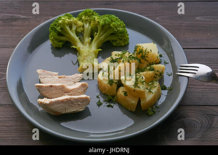 Repas quotidien utile sain le Brocoli bouilli et de pommes de terre poulet sur une plaque gris sur une table en bois brun foncé prêt à partir de la fourche. Banque D'Images