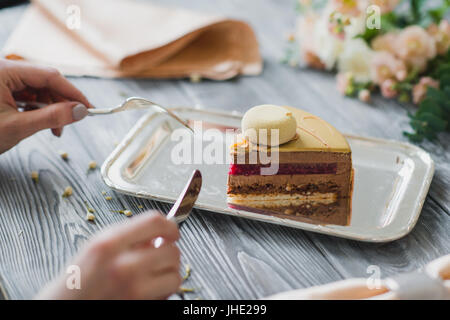 Boulangerie avec morceau de mousse jaune inhabituelle avec dacquoise amande, framboise confit, croustillant de noisettes caramélisées et couche avec poudre de framboise, mousse au chocolat amer sur servi sur table en bois Banque D'Images