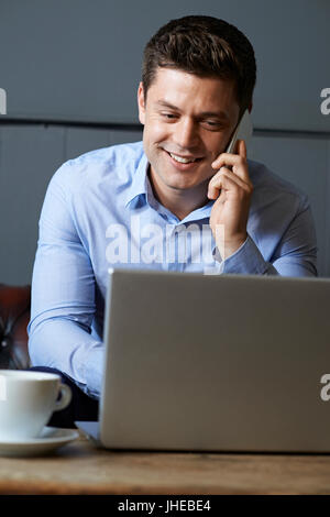 Businessman Talking On Mobile Phone Working On Laptop In Internet Cafe Banque D'Images