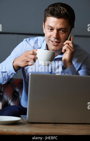 Businessman Talking On Mobile Phone Working On Laptop In Internet Cafe Banque D'Images