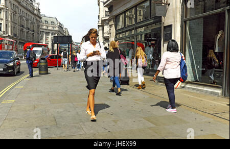 Business Woman promenades le long d'une rue à Londres, en Angleterre, tout en regardant son téléphone portable. Banque D'Images