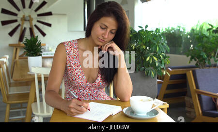 Jeune femme écrivain écrit un livre dans un café. Banque D'Images