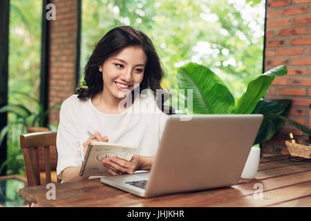 Young smiling woman sitting at table in cafe et écrit dans l'ordinateur portable Banque D'Images