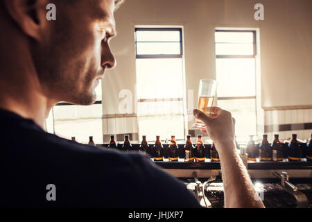 Brewer masculins de la bière artisanale de la brasserie à l'essai en usine. Jeune homme l'examen de l'échantillon au cours de la fabrication de verre de bière. Banque D'Images