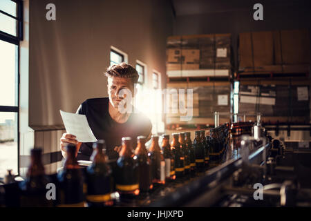 Jeune homme de superviser le processus de fabrication de la bière de la brasserie de l'usine. Travailleur de l'usine contrôle le processus sur la ligne de production en brasserie. Banque D'Images