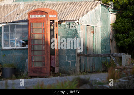 Une vieille et mal aimés abandonnés désaffectées boîte de téléphone rouge se tient à côté de l'abandon d'un immeuble délabré Banque D'Images