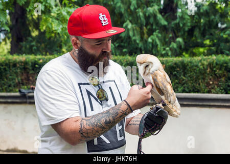 Hipster caucasienne barbu en rouge avec capuchon complet tatouage sur son bras est titulaire d'un hibou dans la main en été sur le s Banque D'Images