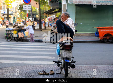 Un chauffeur de taxi moto vietnamienne lit un journal assis sur sa moto à Ho Chi Minh Ville, Vietnam Banque D'Images