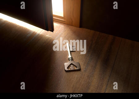 Le rendu 3D de rusty key vintage pose sur plancher en bois en face de alléger porte ouverte Banque D'Images