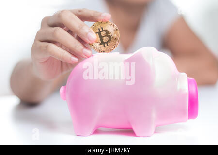 Close up shot of woman putting mains de bitcoin gold pink piggy bank, profondeur de champ, sélectionnez focus on hand Banque D'Images