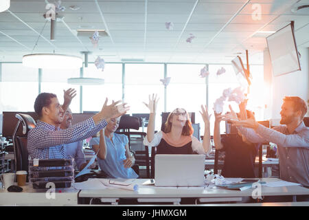 Les gens d'affaires gaie de lancer des boules de papier froissé at desk in office Banque D'Images