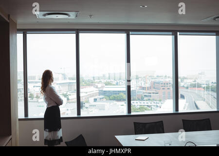 Vue de côté businesswoman looking out à travers le hublot en verre tout en se tenant à l'office de tourisme Banque D'Images