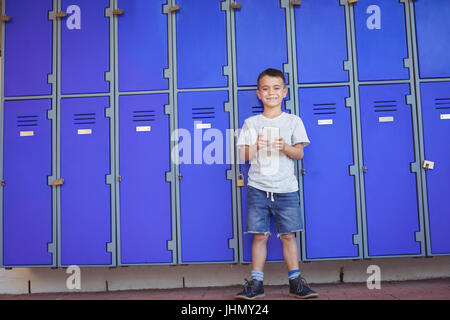 Portrait of smiling boy using mobile phone debout contre les casiers à l'école Banque D'Images