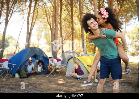 Woman kissing man piggybacking tout en se tenant au camping Banque D'Images