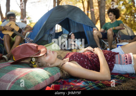 Young woman sleeping while amis assis en arrière-plan de camping Banque D'Images