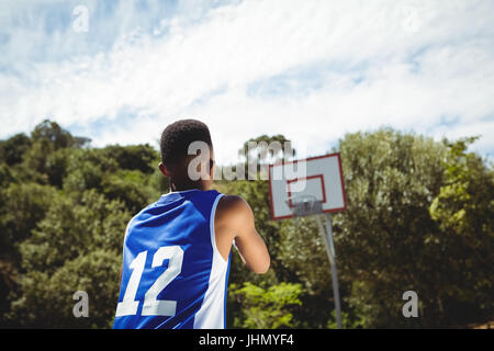 Vue arrière de l'adolescent de sexe masculin pratiquant le basket-ball en cour le jour ensoleillé Banque D'Images