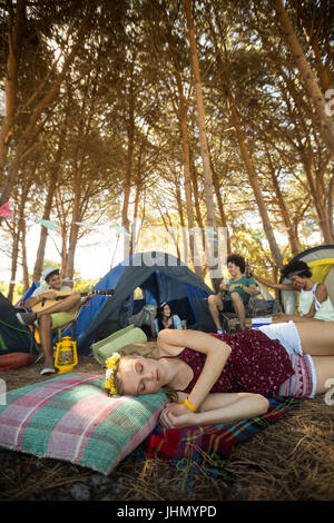 Jeune femme dormir tout en bénéficiant d'amis en arrière-plan de camping Banque D'Images