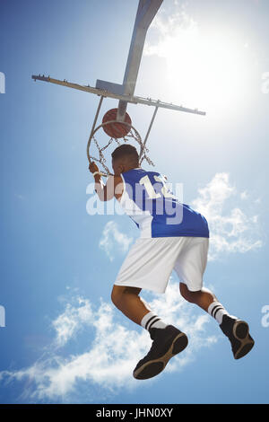 Vue arrière de l'adolescent mâle pendaison le panier de basket-ball against blue sky Banque D'Images