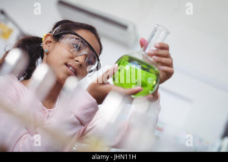 Low angle view of Elementary Student holding green produit chimique dans bécher en verre au laboratoire scientifique. Banque D'Images