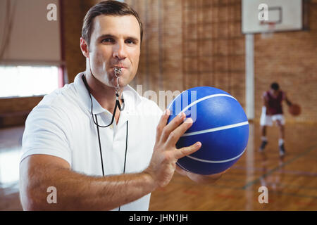 Portrait de coach sifflement tout en maintenant en cour de basket-ball Banque D'Images