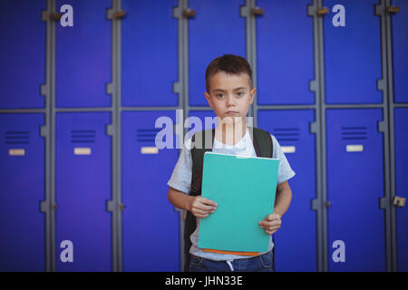 Portrait of boy holding books debout contre les casiers à l'école Banque D'Images