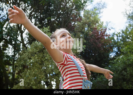 Low angle view of smiling girl with arms outstretched standing contre des arbres à l'arrière-cour Banque D'Images