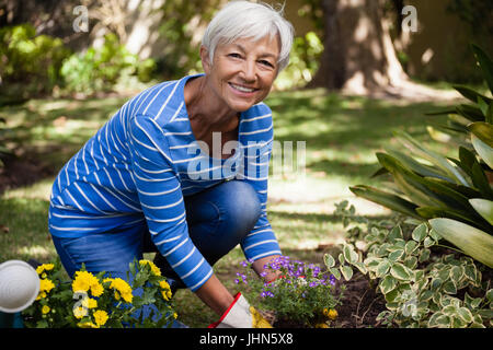 Portrait of senior woman kneeling alors que planter des fleurs dans la cour Banque D'Images