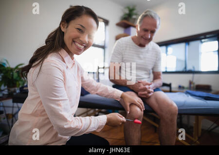 Portrait of female therapist examinant de genou senior male patient avec marteau à réflexe à l'hôpital Banque D'Images