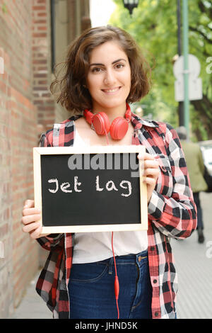 Young Beautiful woman holding tableau avec du texte 'jet lag'. À l'extérieur. Banque D'Images