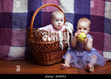 Portrait de deux mignonnes petites filles. Une fille assise dans un panier, la deuxième fille, assis près d'elle et apple rongé Banque D'Images