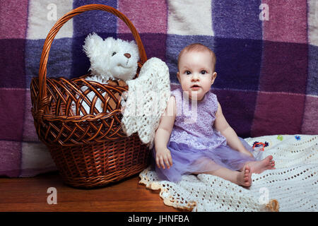 Adorable bébé fille dans une robe lilas assis près de panier en osier Banque D'Images